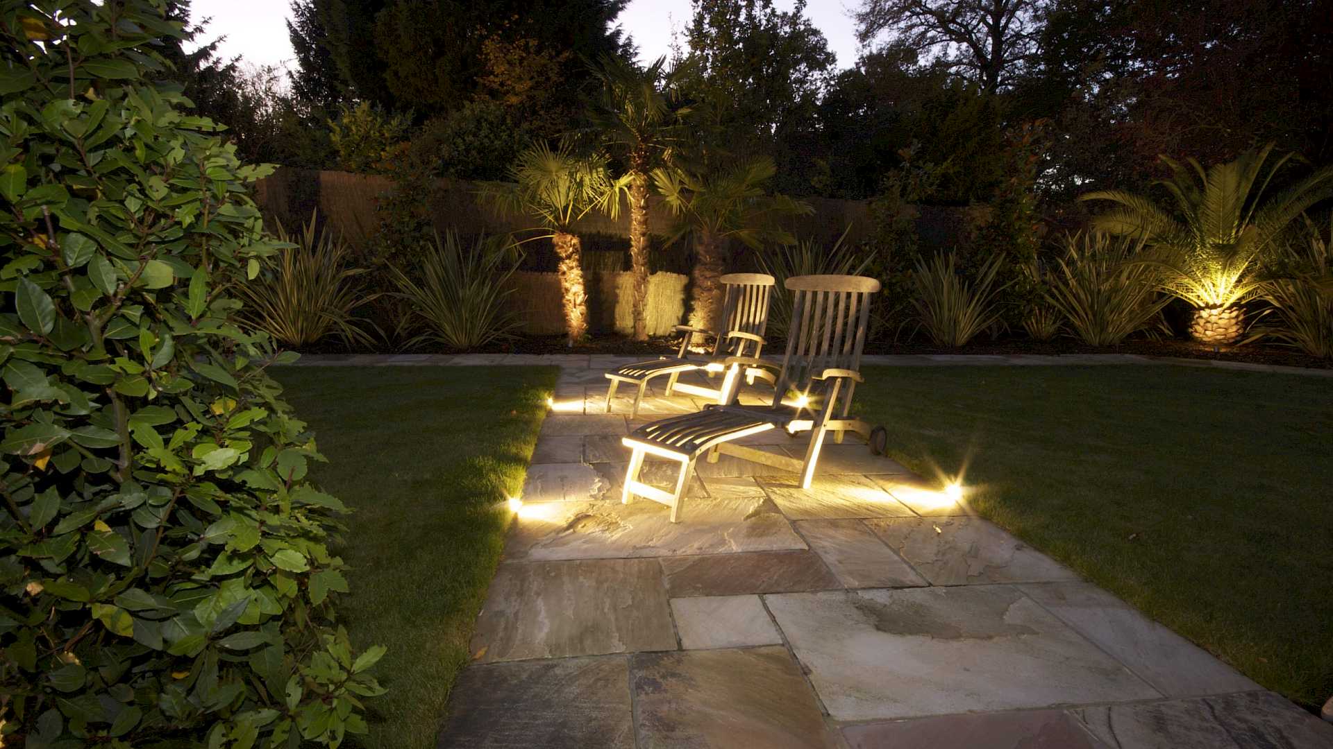 Kent home with Outside Lighting, shows palm trees with uplights and deckchairs with path lights.