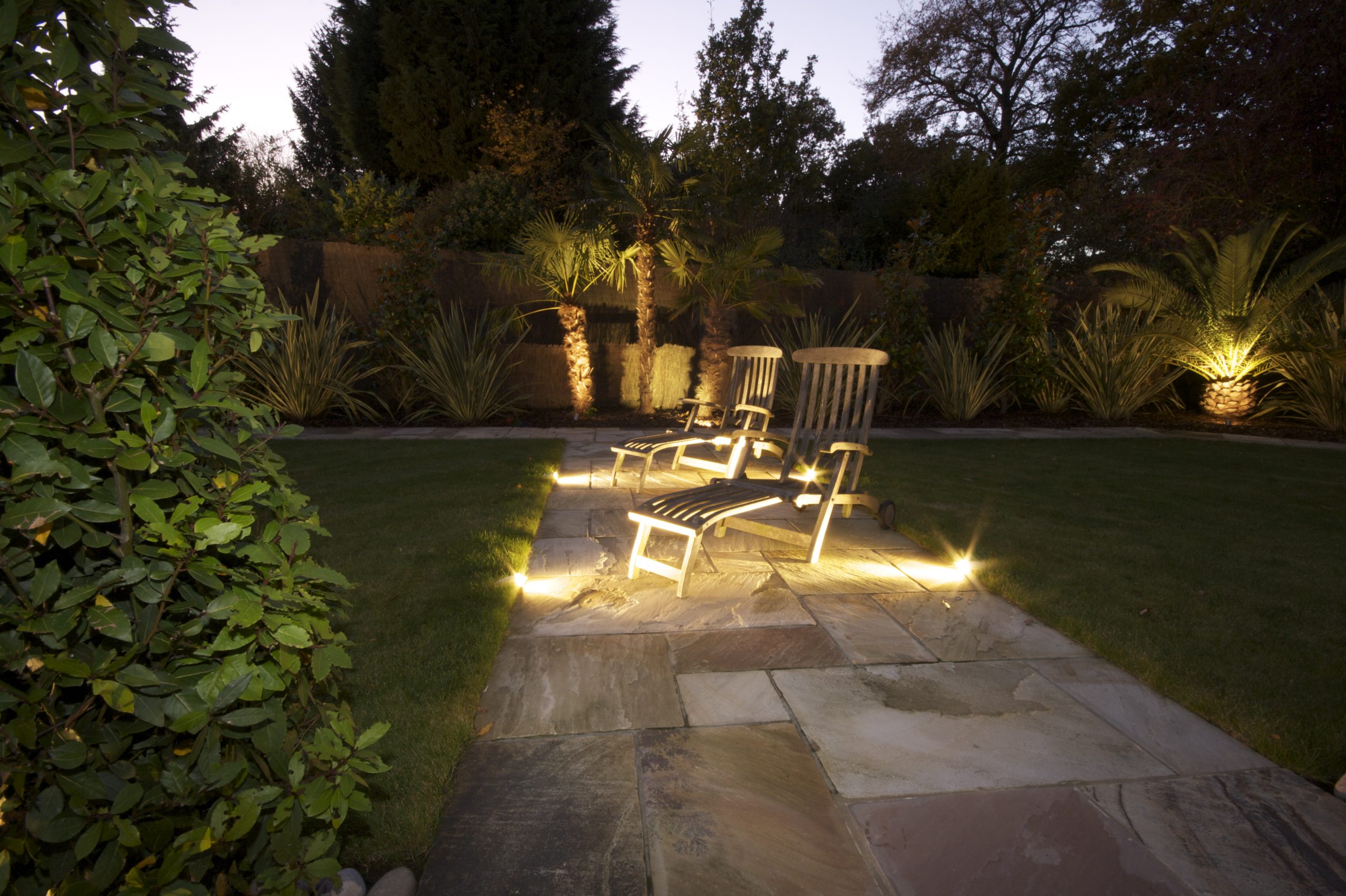 Kent home with Outside Lighting, shows palm trees with uplights and deckchairs with path lights.