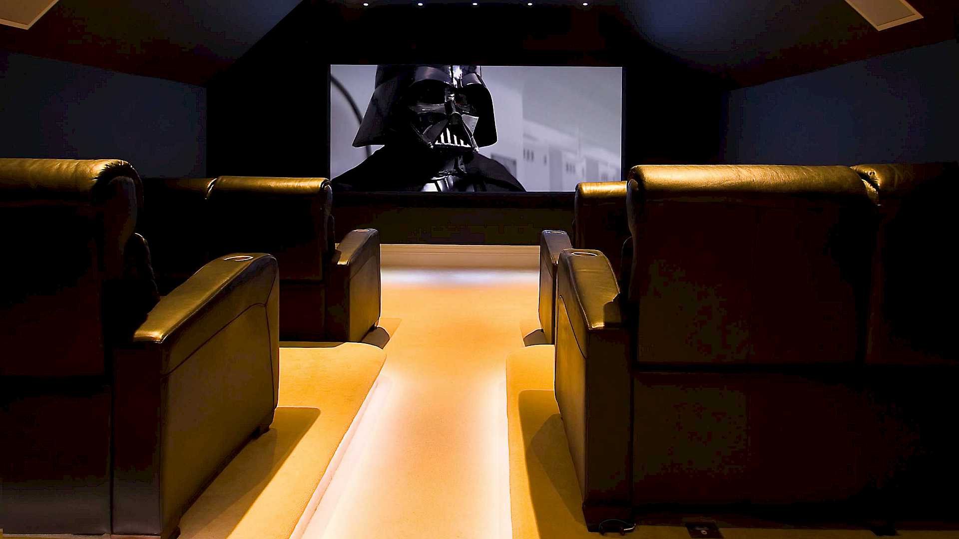 Home cinema above a garage, with low level lighting, cinema chairs and a large screen.