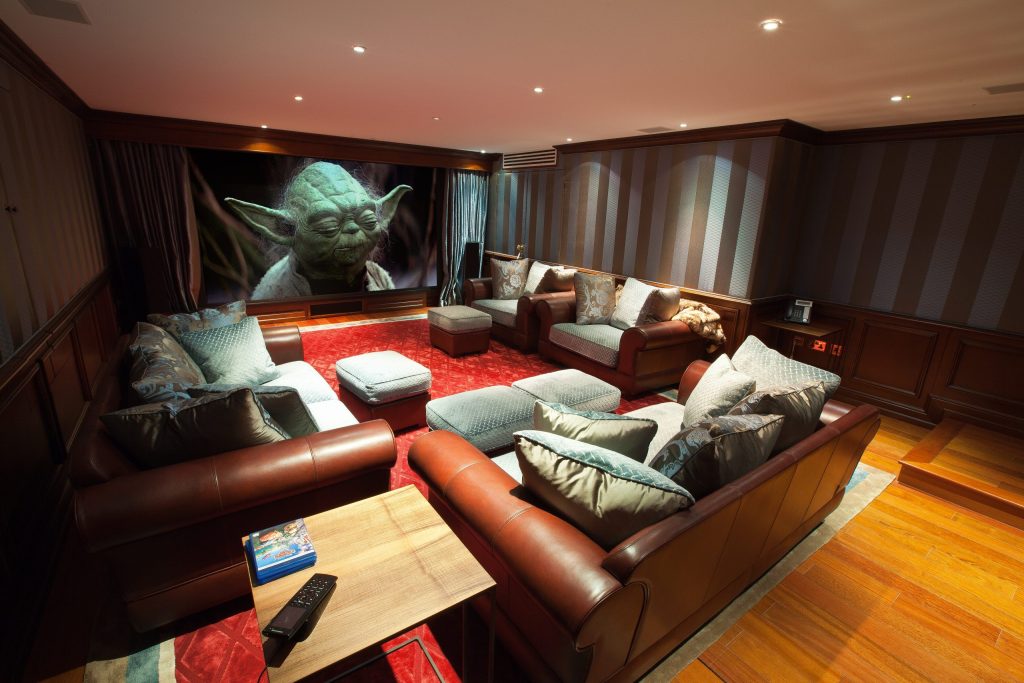 Image shows a media room with Star Wars film showing on the screen. We are often asked how big a home cinema room should be. This room shows what it possible in a multi-use modest space.