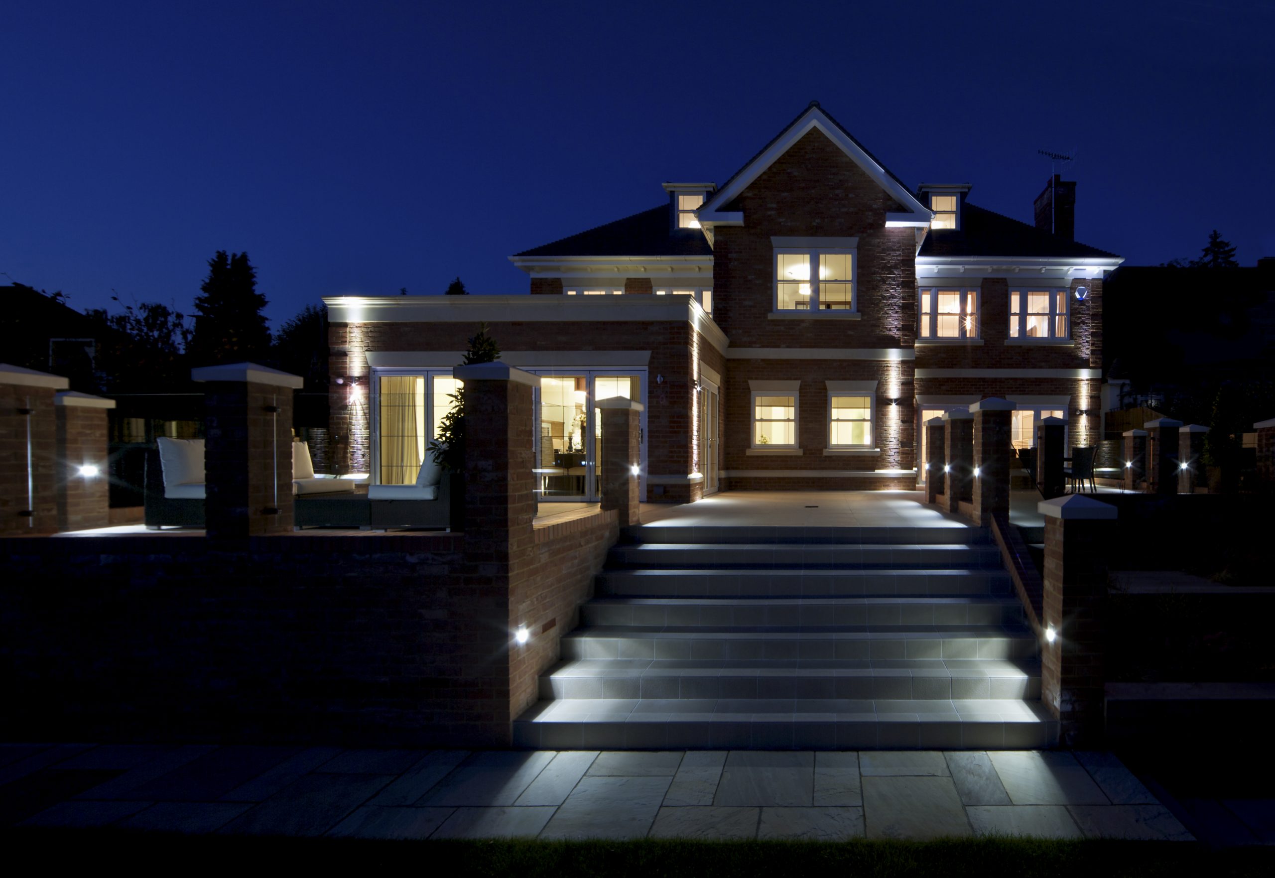 Rear of house with outside lighting and house lights on. Lighting controlled with a system that has had an upgrade to Lutron Homeworks QS.