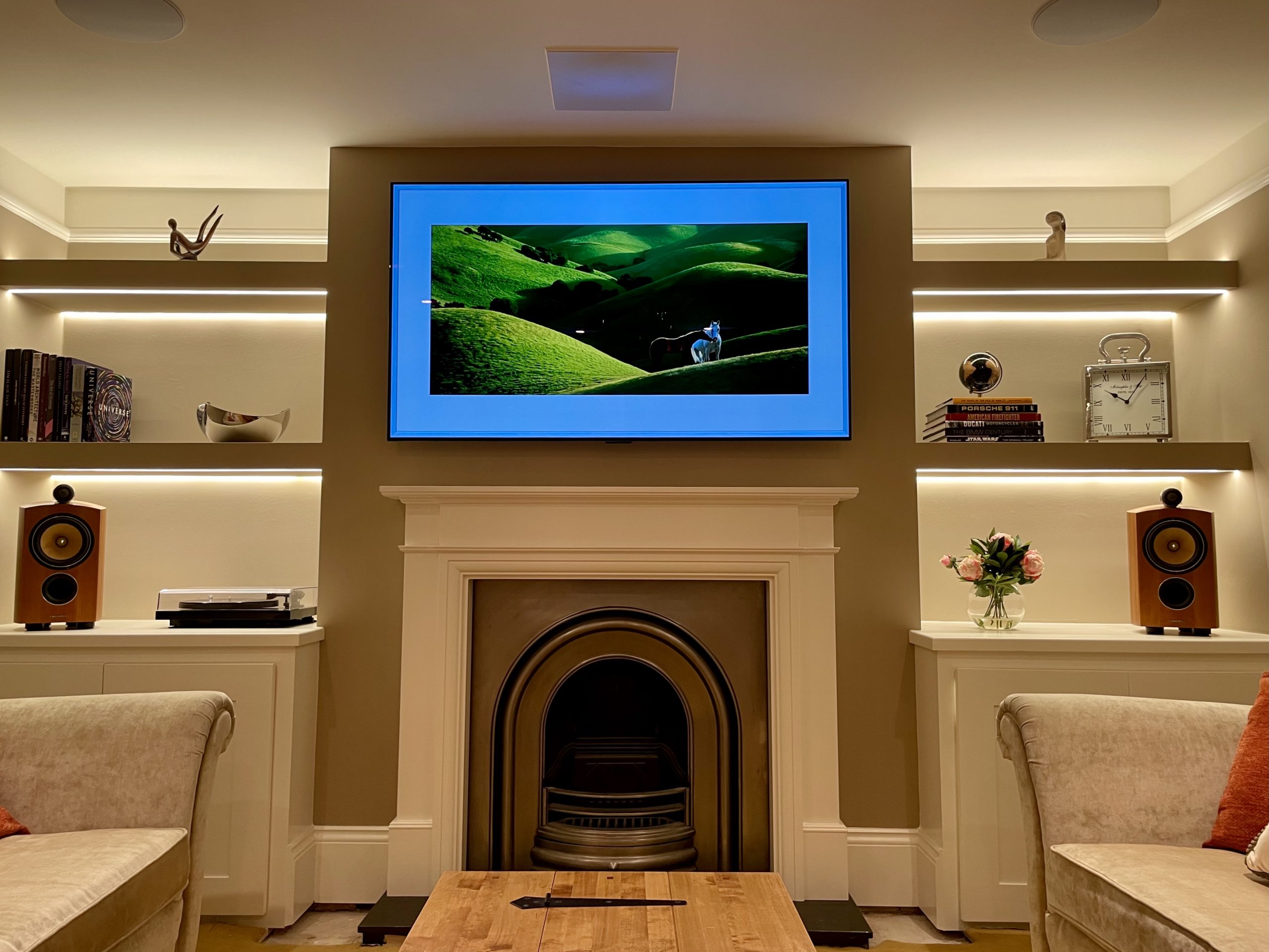 Art screen TV mounted above fireplace on motorised TV bracket in immersive media room.