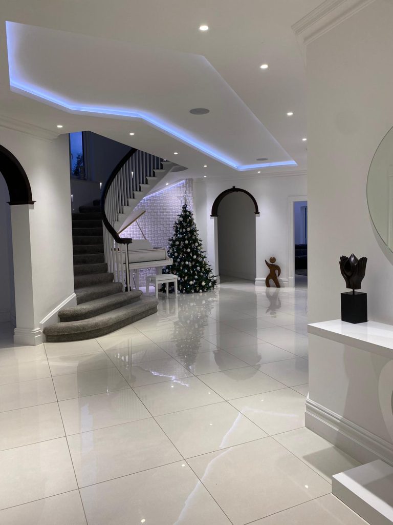 Image shows hallway with Christmas tree, grand piano and lighting Lutron install.