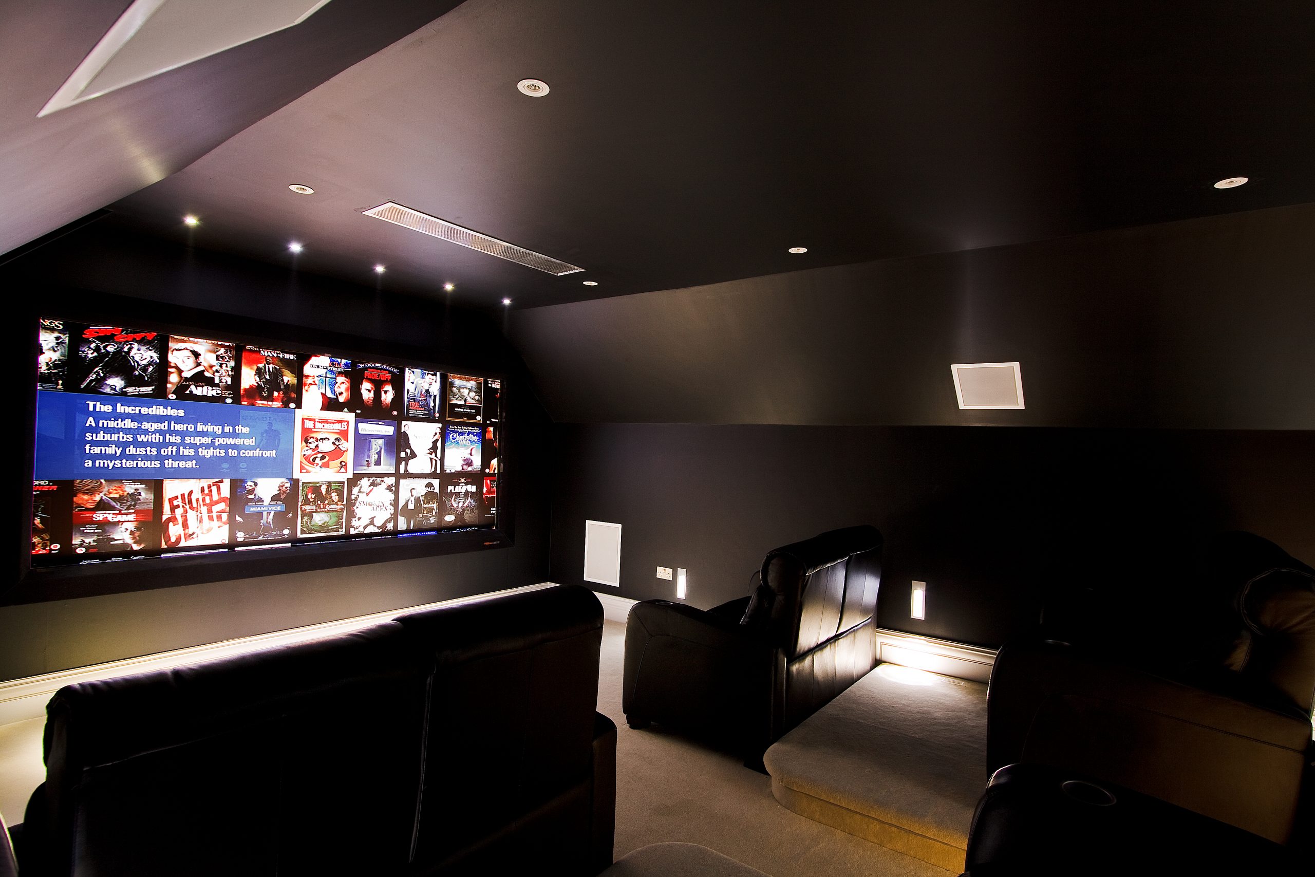 Shows home cinema from side left, with comfortable cinema seating and large acoustically transparent movie screen.